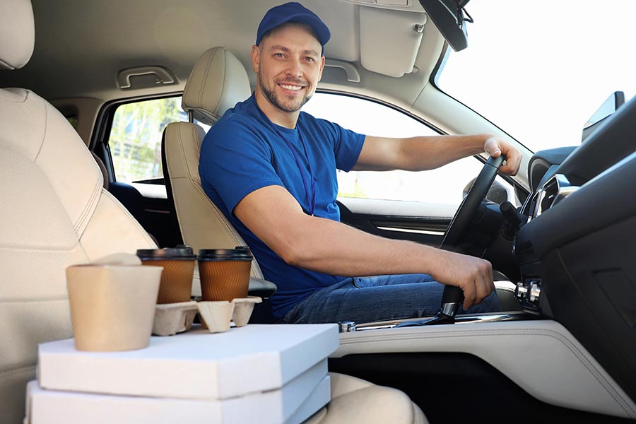 Food Delivery Driver Wearing Blue Shirt, Driving His Car, Food Packages Sitting on the Passenger Seat